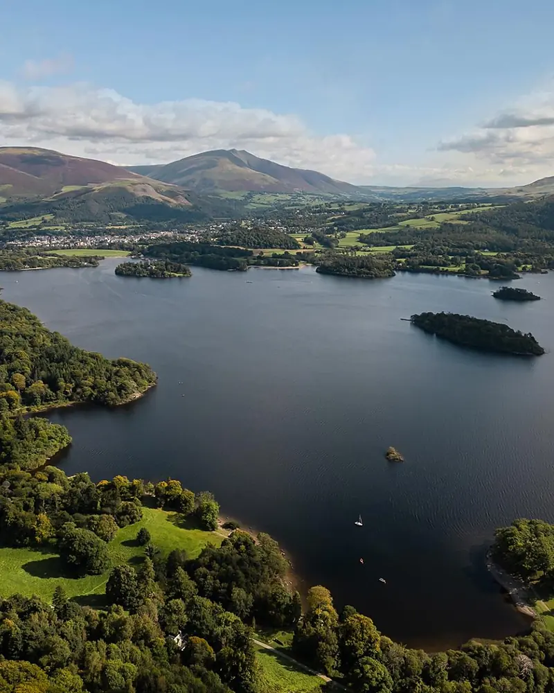 A Lake District valley from the air, with a long lake, wooded islands and the fells rising behind.
