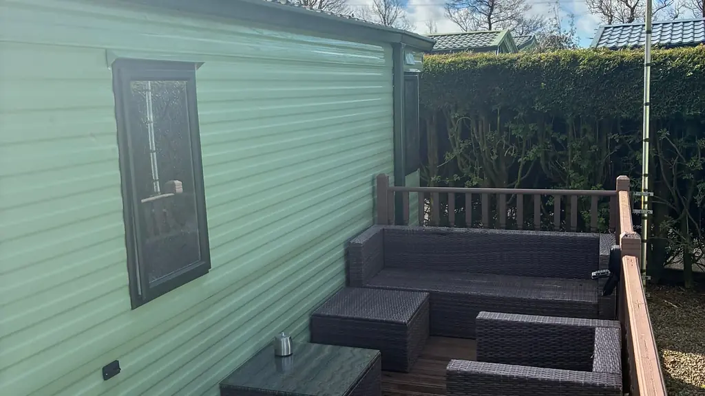 Decking outside one of the caravans with rattan garden furniture and a hedge behind.