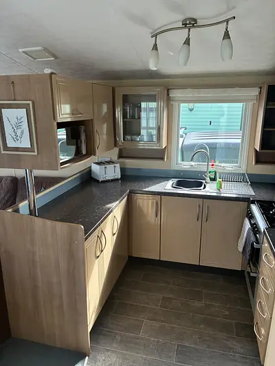 The kitchen in The Lake District Caravan with a dark worktop and blue splashback.