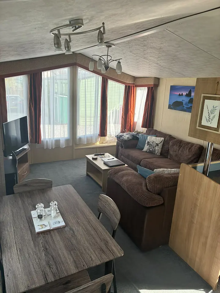 The lounge and dining area in The Lake District Caravan, with a brown corner sofa, blue cushions and a table for six.